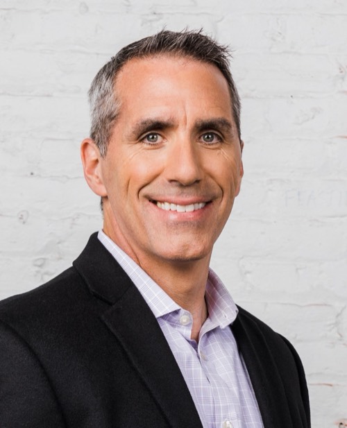 Greg Williams, smiling, in a dark suit jacket.